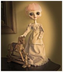 Sepia photo of doll dressed in frontier-style dress with rocking horse