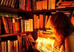 Standing among bookshelves, a woman holds an open book with bright lights shooting out of it